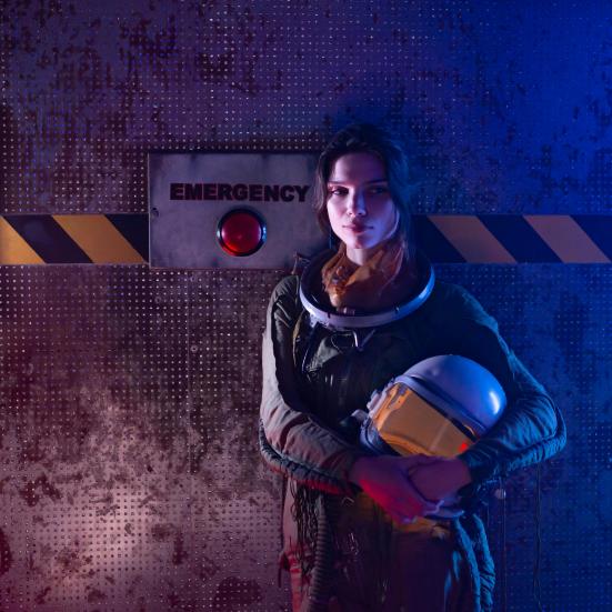 En kvinde iført rumdragt står foran en rød emergency knap