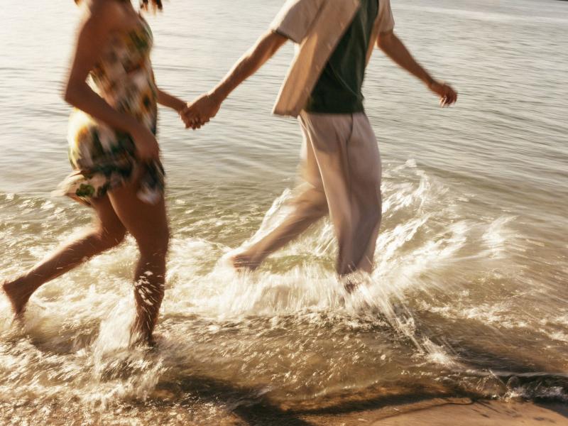 Et par på stranden holder hinanden i hånden mens de løber langs vandkanten.