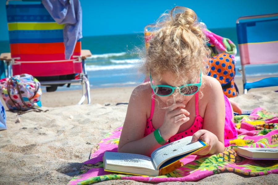 Pige ligger på stranden og læser